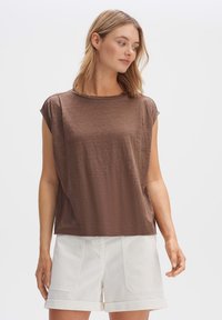 Top marrone a maniche corte con scollo rotondo, texture morbida e vestibilità ampia. Abbinato a pantaloni corti bianchi con orli arrotolati.