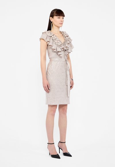 Robe en rose scintillant à manches courtes, avec un col à volants superposés et une ceinture à la taille ; accompagnée de talons aiguilles noirs et de délicates boucles d'oreilles.