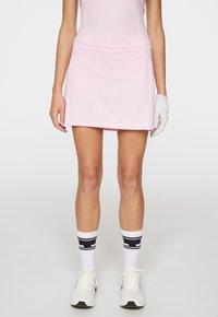 Rosa Sportrock mit glatter Textur und breitem Bund. Kombiniert mit weißen Schuhen und knielangen Socken mit schwarzen Akzenten.