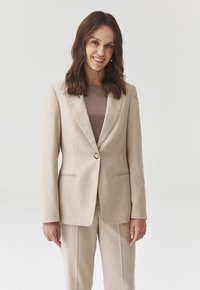 Béžový požadovaný blazer se strukturálními klopami a zapínáním na jeden knoflík, texturovaná látka, spárovaný s odpovídajícím béžovým topem.