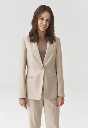 Béžový požadovaný blazer se strukturálními klopami a zapínáním na jeden knoflík, texturovaná látka, spárovaný s odpovídajícím béžovým topem.