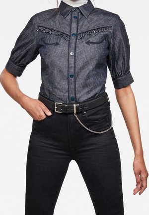 Mørk denim kortærmet skjorte med flæsedetalje foran og blå knapper, kombineret med sorte bukser, sort bælte og sølvkædeaccessory.