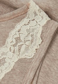 Ljusbrun ribbad tyg med en krämfärgad spetssnell längs halsringningen, med ett blommönster och vågiga kanter.