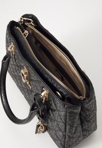 Sac à main noir à motifs avec deux poignées supérieures, garnitures en métal doré, et ouverture supérieure dévoilant un intérieur beige avec compartiments zippés.