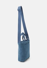 Blue fabric tote bag with a structured shape. Features a long, adjustable strap and two small top handles for carrying convenience.