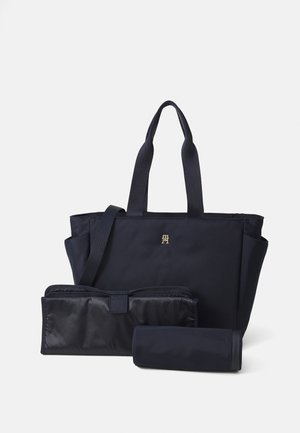 Sac fourre-tout bleu marine avec poignées doubles, arborant un logo doré et deux poches séparées : une élégante et une plus grande avec une fermeture éclair.