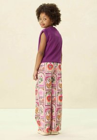 Top sans manches violet associé à un pantalon large à motifs, avec des cœurs colorés et des motifs floraux sur fond clair.