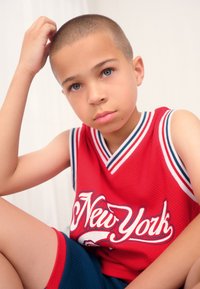 Red mesh basketball jersey with white and blue accents, featuring "New York" text. Worn with blue athletic shorts, against a light background.