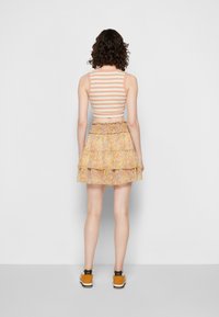 Top cropped listrado em pêssego e branco; saia floral em camadas com bainha rodada em amarelo, rosa e roxo; modelo a usar ténis.