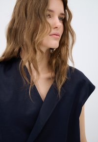 Marinblå, kortärmad topp med V-ringning och en jämn textur. Avslappnad passform med en strukturerad halsringning och minimal detaljering.