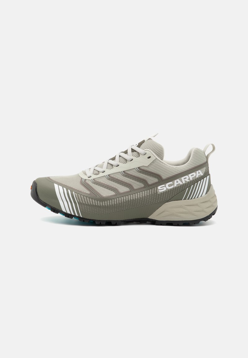 Lichtgrijze trailrunningschoen met een gestructureerde mesh bovenkant, donkergrijze accenten, gestreepte details en een zwarte rubberen loopzool voor grip.