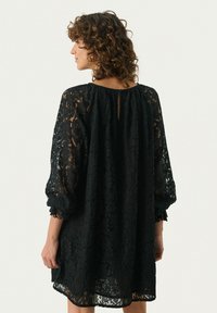 Schwarzes Spitzenkleid mit Dreiviertelärmeln, rundem Ausschnitt und kleinem Rückenausschnitt; texturiertes florales Muster über das gesamte Kleid.
