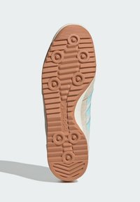 Semelle de sneaker en caoutchouc brun clair, avec de profondes rainures et des motifs circulaires, des accents bleu clair et un dessus beige texturé.