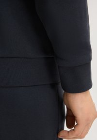 Felpa blu navy con texture a coste, maniche con polsini e vita aderente. Il tessuto appare morbido ed elastico.