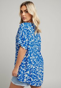 Top oversize blu e bianco con stampa, maniche corte, caratterizzato da una vestibilità rilassata e leggere aperture laterali per maggiore comfort.