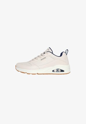 Baskets beige clair avec une tige en cuir lisse, accents bleu marine, design à lacets ronds, col rembourré et amorti d'air visible dans la semelle.