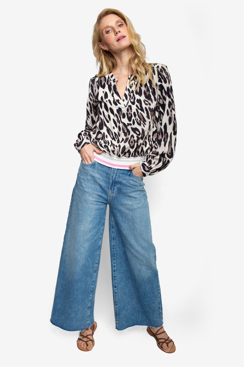 Blouse met luipaardprint, een V-hals en opgeblazen mouwen, gecombineerd met wijd uitlopende lichtblauwe spijkerbroeken en bruine sandalen met bandjes.