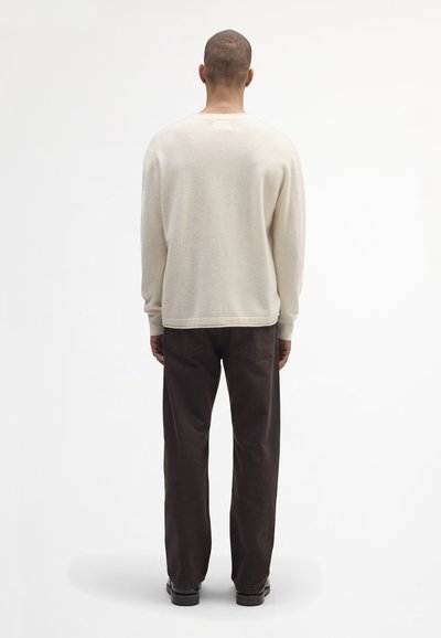 Hellbeige Pullover mit einer lockeren Passform, gerippten Bündchen und Saum. Kombiniert mit dunkelbraunen Hosen, die beide ein minimales Design und keine Muster aufweisen.