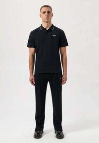 Svart polo med kontrasterande vita ränder på kragen, kombinerad med svarta byxor, båda med en mjuk textur och minimalistisk design.