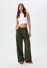 Weite olivgrüne Hosen mit Falten und einem Gürtel, kombiniert mit einem enganliegenden weißen Cropped-Top. Sanfter Stoff, elegantes Design.