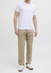 Valkoinen puuvillainen t-paita yhdistettynä beigen värisiin puuvillahousuihin ja valkoisiin lenkkareihin. Yksinkertainen, istuva muotoilu pyöreällä pääntiellä ja lyhyillä hihoilla.