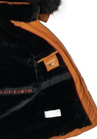 Orange exterior jacket with black fur lining. Features a pocket with a logo tag and a black strap with red text: "NAVAHOO ON EARTH."