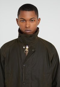 Dark green waterproof jacket with a high collar, zippered front, and snap button closures; features a soft, ribbed interior lining.