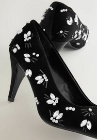 Chaussures à talons hauts en daim noir décorées de grappes de strass blancs et transparents disposés en motifs floraux.