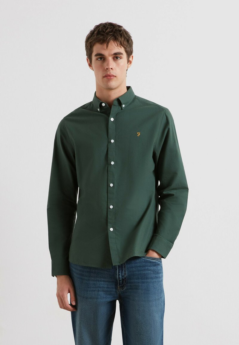 Groene geknoopte shirt van katoen, met een klassieke kraag, witte knopen en een klein geborduurd logo op de borst. Gemaakt in combinatie met blauwe jeans.