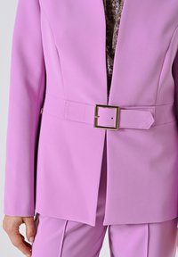 Roze blazer met een gedefinieerde taille en een rechthoekige gouden gespriem, gemaakt van gladde stof met een gestructureerde pasvorm.