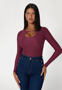 Bordo ilgomis rankovėmis bodis su iškirpimu krūtinės srityje, derinamas su aukšto liemens tamsiai mėlynomis džinsomis su auksiniais mygtukais.