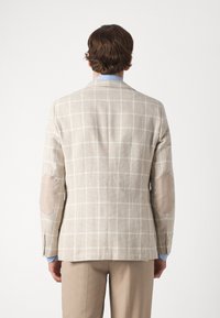 Beżowa marynarka w kratę dla mężczyzn z łatanami na łokciach, wykonana z teksturowanej tkaniny. Posiada zapięcie na dwa guziki oraz klasyczne klapy w kształcie notcha.