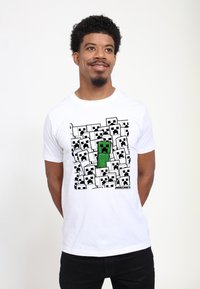Bílý tričko s digitálním potiskem zeleného Minecraft Creepera obklopeného několika bílými tvářemi Creepera, s černými konturami.