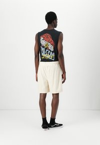 Sort ærmeløs grafisk tanktop med farverigt design, parret med lyse teksturerede shorts og sorte sneakers med hvide accenter.
