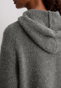 Szary polarowy sweter z kapturem, miękka tekstura, luźny krój, widoczne szwy i zaokrąglony design kaptura, co zapewnia przytulny wygląd.