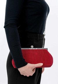 Clutch bag plissettato rosso con una cornice argentata e un fermaglio decorativo, portato a mano; il tessuto ha una superficie texture e una forma arrotondata.