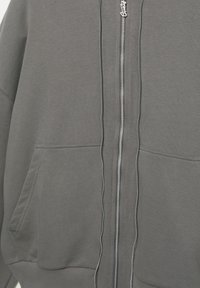 Felpa con cappuccio grigia con zip, caratterizzata da una texture liscia, due tasche frontali e una zip argentata con dettaglio del marchio sul cursore.