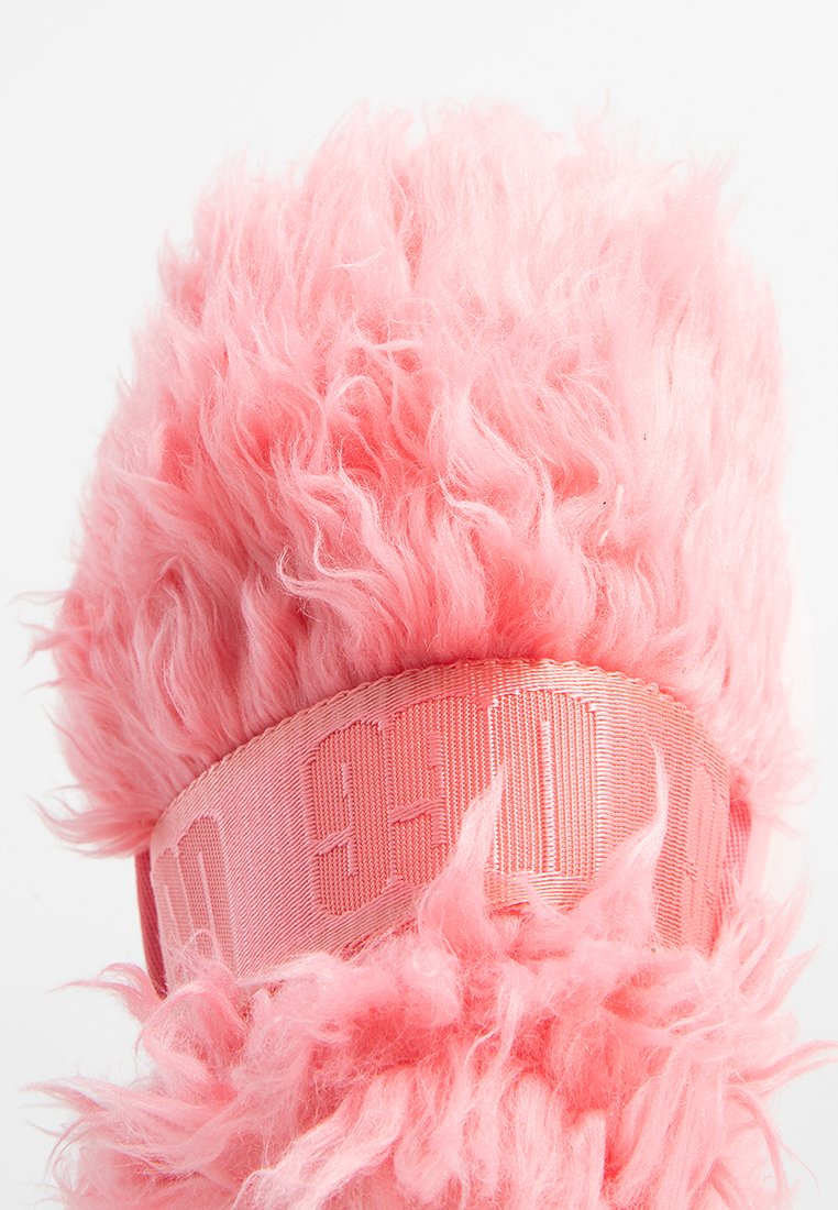 Prodotto rosa peloso con finitura testurizzata e soffice, dotato di una larga fascia rosa con testo impresso. Il design è morbido e di forma circolare.