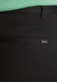 Svarta skräddarsydda byxor i vävt tyg med en jämn textur. Har en sidoficka och en liten "Polo"-etikett på midjebandet.