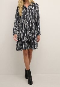 Abito blu navy con strisce ondulate bianche, maniche lunghe, design a strati e colletto. Abbinato a stivaletti neri alla caviglia.