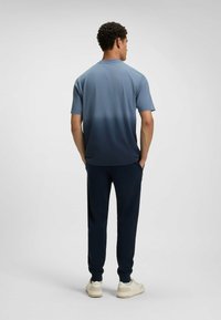 T-shirt da uomo a maniche corte in blu, che sfuma fino a un blu navy scuro, abbinato a pantaloni navy scuro e sneakers di colore chiaro.