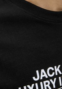 Svart bomull t-shirt med rundad halsringning, med fet vit text som säger "JACK" och "LUXURY IN". Slät textur med hållbar sömnad.