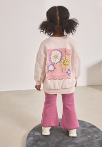 Light pink sweatshirt with colorful celestial graphics on the back, paired with pink flared pants and white footwear. Text reads "LOOK AT THE STARS IN THE SKY."