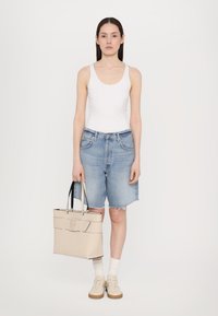 Heledad teksast sinises värvitoonis denim lühikesed püksid, mille servad on kulutatud, koos lihtsa valge topi ja beeži kottiga, millel on mustad käepidemed ja logo detail.