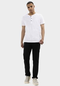 Biała, krótko rękawowa koszulka henley z trzema czarnymi guzikami, w zestawie z czarnymi spodniami i jasnoszarymi sneakersami. Gładki materiał, casualowy krój.