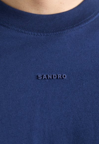 T-shirt in cotone blu navy con colletto a girocollo a coste e un logo in gomma testurizzata blu scuro con la scritta "SANDRO" sul petto.