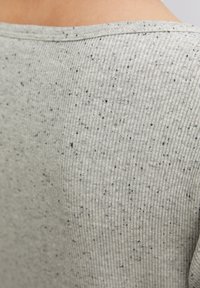 Tessuto grigio a coste con sottili strisce testurizzate e macchie nere sparse. Lo scollo è ampio e rotondo.