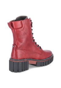 Red leather ankle boot with a lace-up design, padded collar, and thick black rubber sole featuring ridged detailing and contrasting stitching.