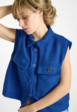 Blue textured sleeveless vest with a collared neck, front pockets, button closure, and a gold hardware accent.