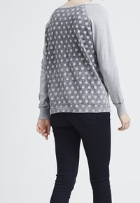 Suéter gris con un patrón de puntos en la parte posterior, mangas contrastantes y puños acanalados. Textura suave, corte casual, combinado con pantalones oscuros.